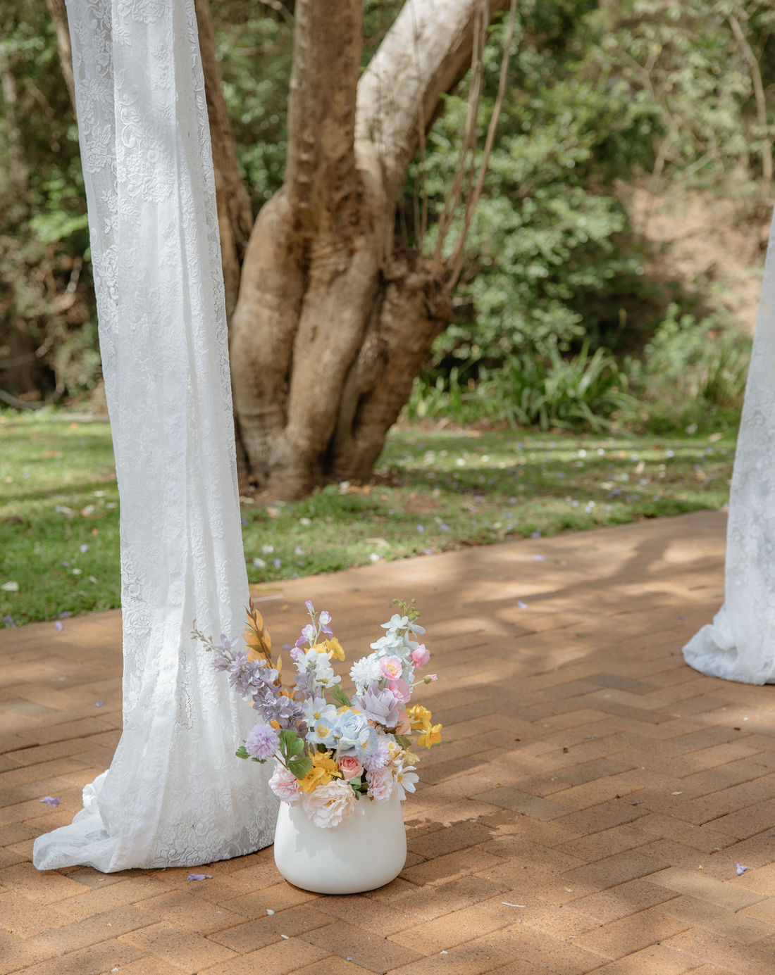 Sheer white ceremony draping with a pastel silk posy in a white vase beside the aisle