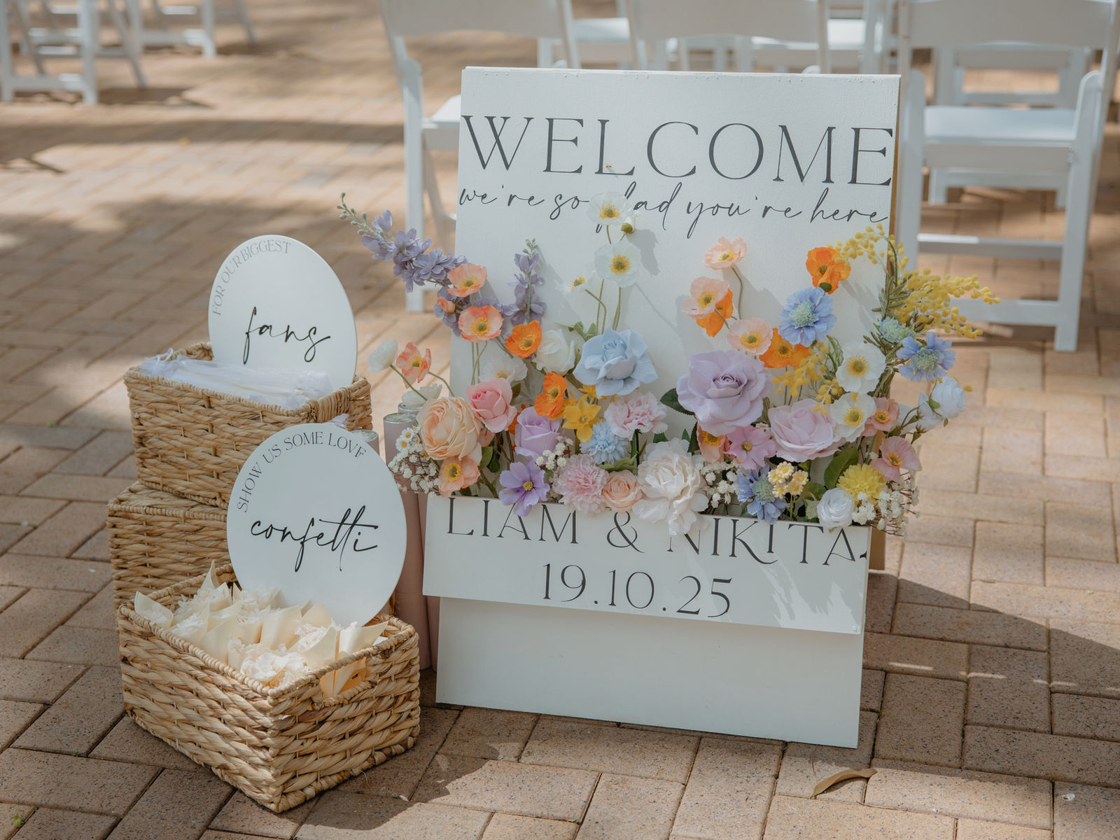 Personalised welcome sign with a meadow style silk arrangement of poppies, stock, roses and wattle beside a confetti basket