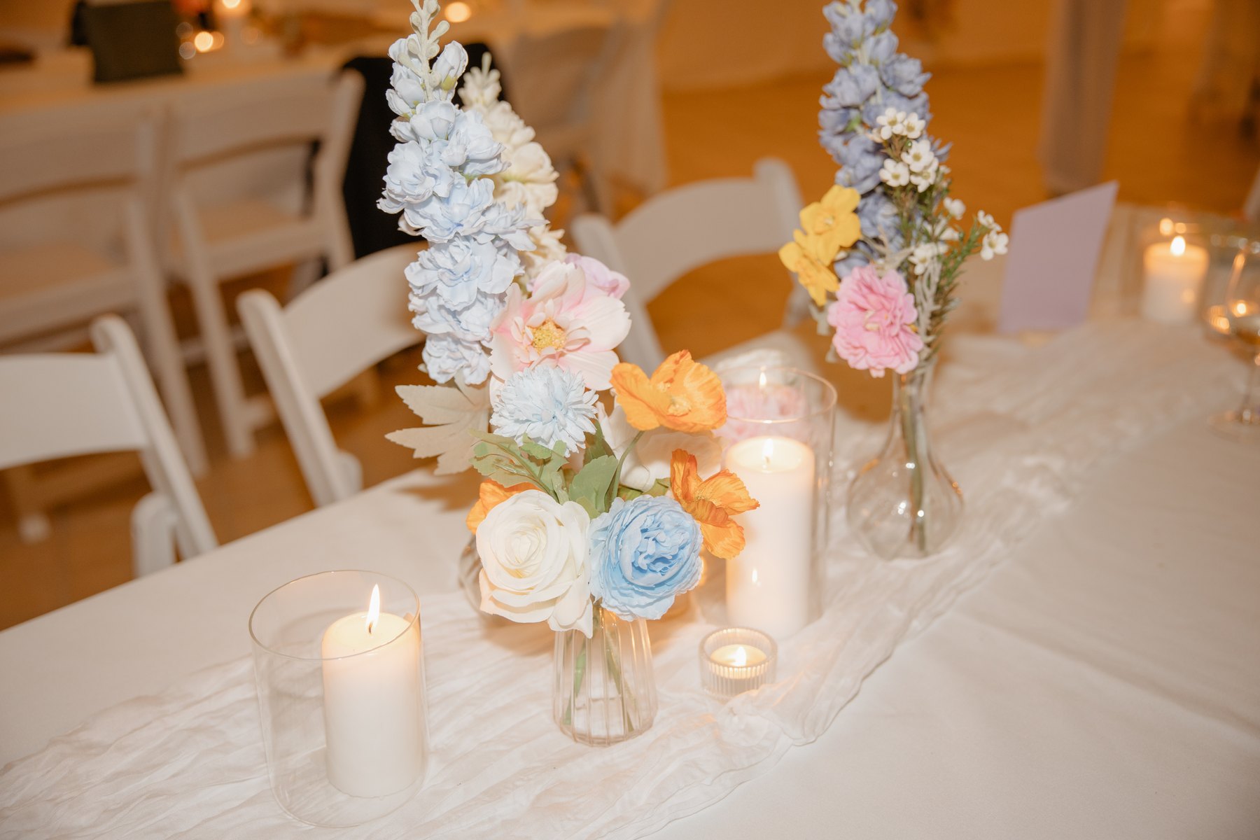 Candlelit reception table styled with colourful silk florals, taper candles and warm glassware