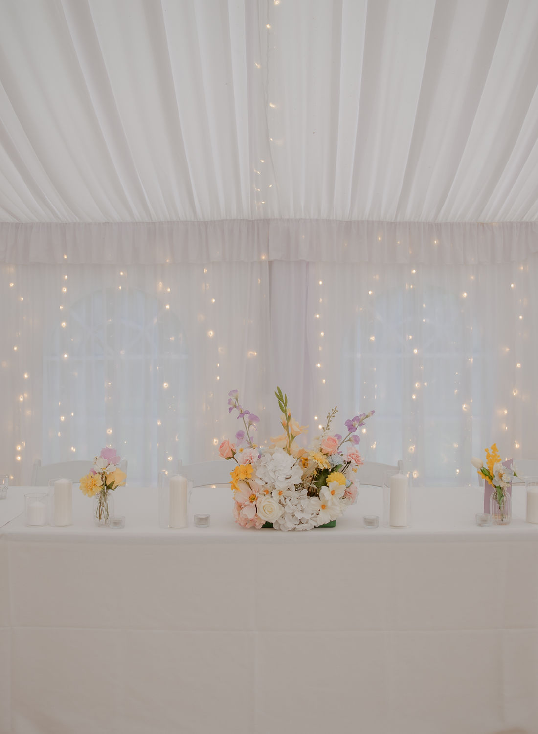Reception tables styled with soft pastel bud vases, candles and fairy lit draping