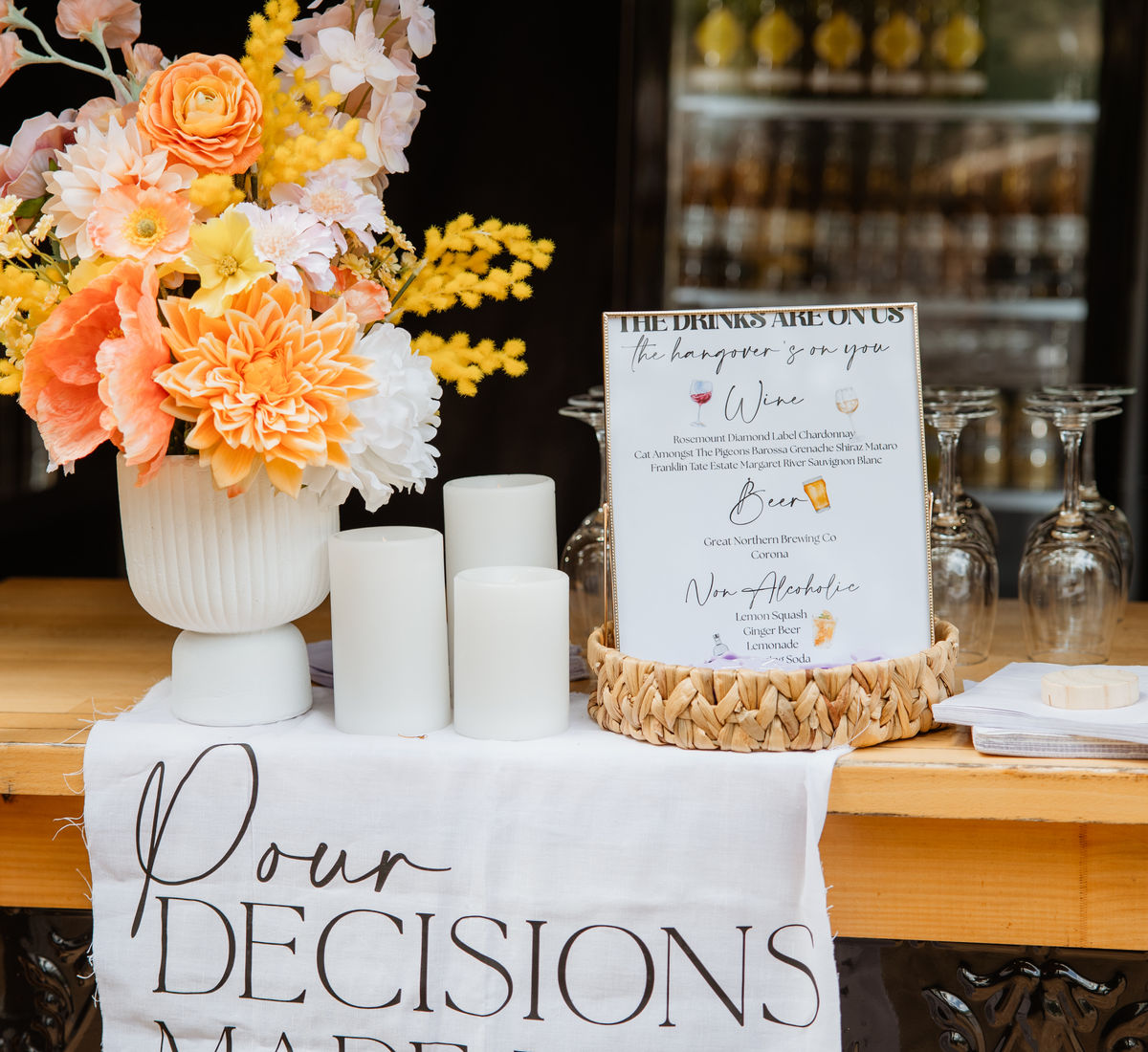 Bar styled with coral roses, an orange dahlia, mustard wattle, pillar candles and a personalised drinks sign